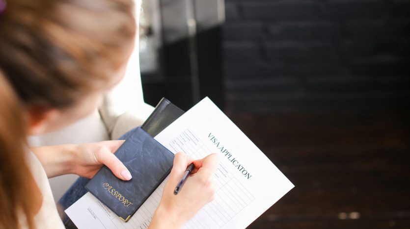 Une personne remplissant un formulaire de demande de visa avec un passeport en main, se concentrant sur le document posé sur une table en bois dans une villa de Dubaï.