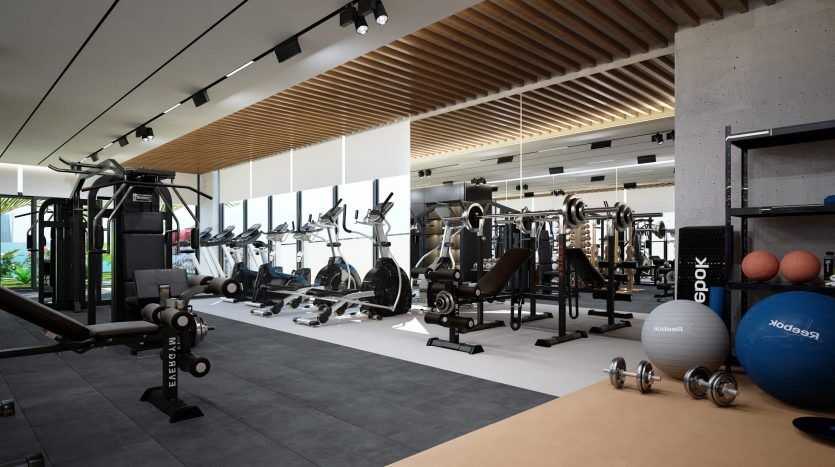 Intérieur de salle de sport moderne dans une villa de Dubaï avec une variété d'équipements de fitness, notamment des tapis roulants, des appareils d'haltérophilie et des ballons d'exercice. L'espace présente des poutres en bois au plafond et de grandes fenêtres.