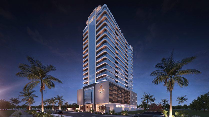 Un immeuble moderne de grande hauteur à Dubaï illuminé au crépuscule, doté de balcons bien éclairés, d'une entrée élégante et entouré de palmiers et d'un ciel nocturne dégagé.