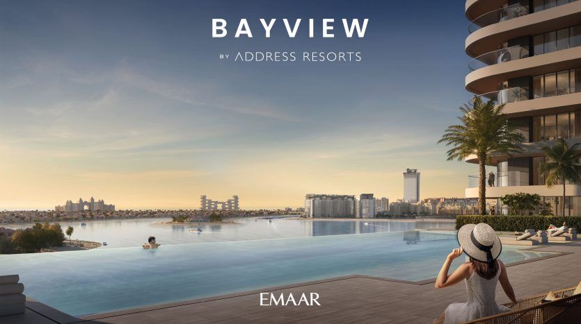 Une femme portant un chapeau à larges bords est assise au bord d'une piscine à débordement surplombant un paysage urbain côtier pittoresque au coucher du soleil, avec le texte « bayview by address resorts » et « immobilier dubai »