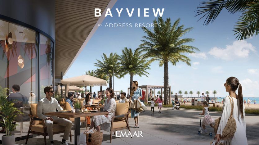 Coin salon luxueux avec des gens socialisant autour de tables donnant sur une plage bordée de palmiers sous un ciel bleu clair, dans le cadre de l'image promotionnelle du complexe Bayview by Address mettant en vedette un appartement haut de gamme à Dubaï