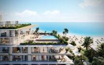Una lujosa villa frente al mar en Dubai con terrazas de varios niveles, piscina infinita y ordenadas hileras de tumbonas en una playa de arena, con vistas a un vasto océano azul bajo un cielo despejado.