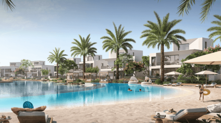 Un complejo de lujo en Dubai con modernos edificios blancos, frondosas palmeras y una gran piscina. La gente se relaja en tumbonas bajo sombrillas y disfruta de un día soleado.