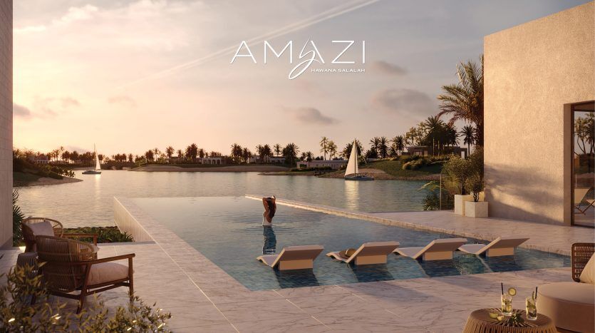 Une personne se tient au bord d'une piscine à débordement surplombant un lac serein avec un voilier au coucher du soleil, entourée d'une végétation luxuriante et d'un mobilier d'extérieur moderne, arborant le logo « amazi » et la marque