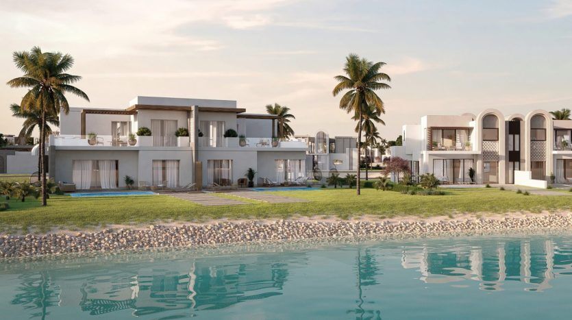 Villas de luxe modernes en bord de mer à Dubaï avec de grandes fenêtres et balcons donnant sur un étang de réflexion tranquille, flanqué de palmiers sous un ciel clair.