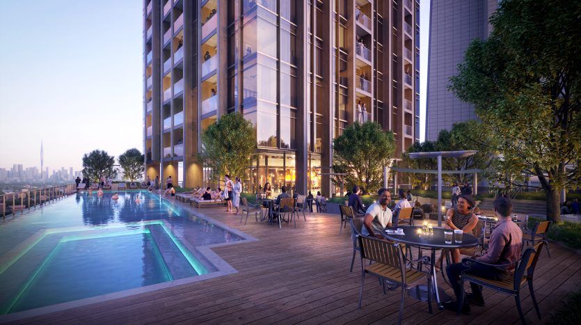 Les gens dînent et socialisent sur une terrasse éclairée au bord d'une piscine à débordement dans un appartement moderne de grande hauteur à Dubaï en soirée, avec un horizon de la ville en arrière-plan.