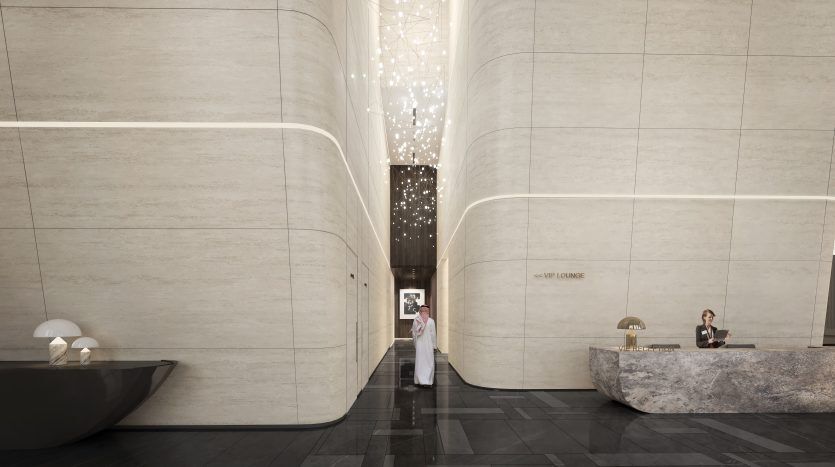 Un hall d'hôtel moderne à Dubaï avec de hauts plafonds incurvés et d'élégants murs en marbre. Un lustre central descend et un homme en tenue traditionnelle passe, accueilli par un réceptionniste assis à un bureau en pierre.