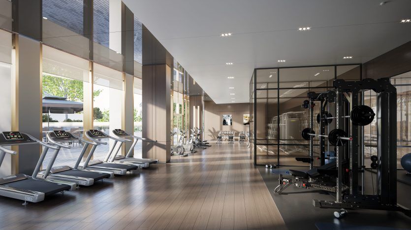 Un intérieur de salle de sport moderne comprenant des tapis roulants alignés près de grandes fenêtres avec beaucoup de lumière naturelle, des appareils de musculation et un espace vitré avec des vélos en arrière-plan, le tout situé dans une propriété de premier ordre de Dubaï.