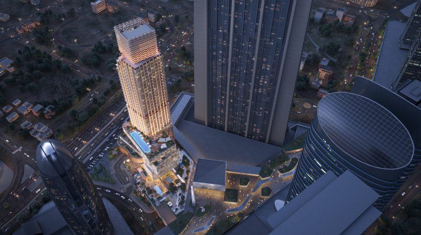 Vue aérienne nocturne d'un paysage urbain moderne de Dubaï avec des gratte-ciels illuminés, des routes et une zone urbaine animée, mettant en valeur la diversité architecturale et la vie urbaine animée.
