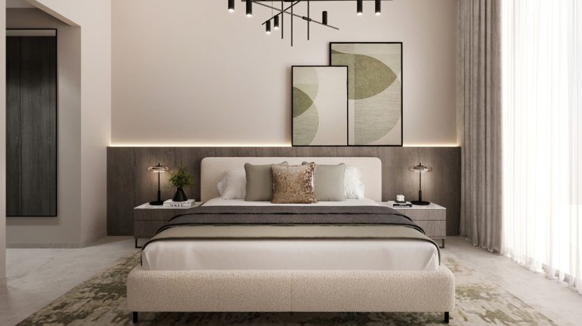 Une chambre moderne dans un appartement de Dubaï avec un grand lit doté d'une literie blanche et grise, flanqué de tables d'appoint et de lampes en bois, contre un mur rose clair avec des œuvres d'art abstraites au-dessus de la tête de lit.
