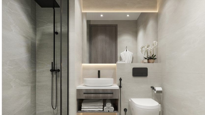 Intérieur de salle de bains moderne comprenant un meuble en bois avec un lavabo blanc, un miroir, des toilettes murales et une douche à l'italienne dans un appartement de Dubaï, accentué par des carreaux de pierre grise et un éclairage chaleureux