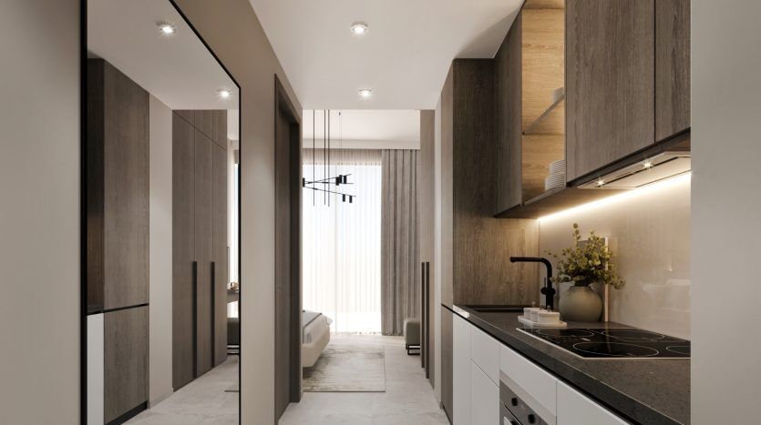 Intérieur de cuisine moderne avec armoires en bois élégantes, comptoirs blancs et appareils électroménagers intégrés dans un luxueux appartement de Dubaï. Des plafonniers à intensité variable éclairent l'espace menant à une pièce attenante avec une suspension visible