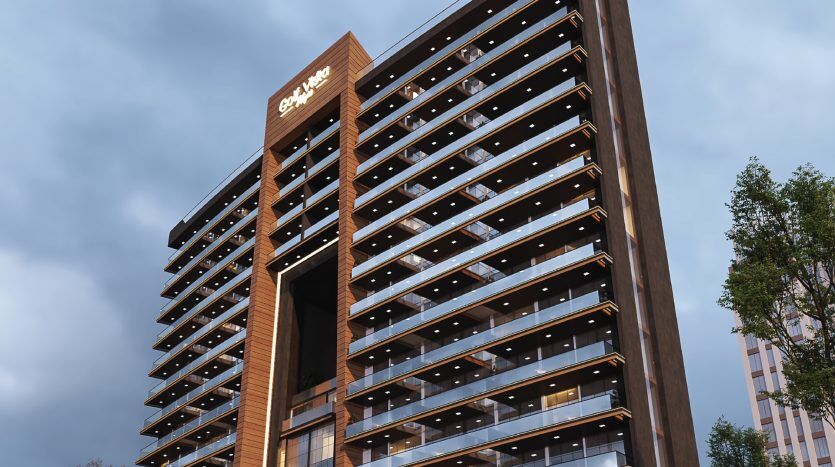 Bâtiment moderne de plusieurs étages à Dubaï avec une façade en bois et une signalisation lumineuse au sommet, vu sous un angle faible. Les lumières sont allumées à de nombreuses fenêtres et des arbres sont visibles sur les bords.
