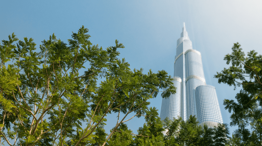 Une vue d'un grand gratte-ciel chatoyant dominant des arbres verdoyants sur un ciel bleu clair, incarnant le premier immobilier de Dubaï.