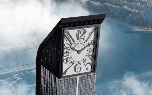 Un grattacielo con un grande quadrante di orologio integrato nella sua sommità, che si affaccia su una città costiera di Dubai parzialmente oscurata dalla nebbia mattutina.