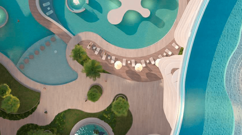 Vue aérienne d'un complexe luxueux doté d'une piscine de forme unique avec des chaises longues, entourée d'une verdure luxuriante et adjacente à un autre plan d'eau à Dubaï.