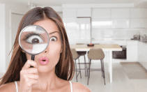 Una mujer sorprendida sosteniendo cerca del ojo una lupa que le agranda considerablemente el ojo, en una moderna cocina de una villa de Dubai.