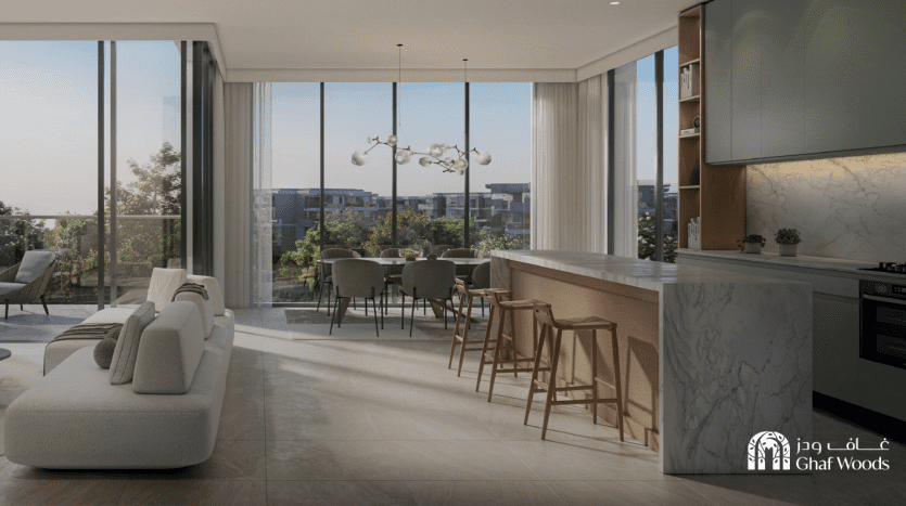 Une cuisine ouverte moderne et un salon doté de grandes fenêtres avec vue sur les bois de ghaf. La cuisine dispose d'un îlot avec des tabourets de bar en bois et le salon comprend un canapé élégant. Les luminaires et les armoires ajoutent au décor contemporain.