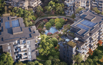 Aerial view of a luxury residential complex comprising several modern apartment buildings, complete with rooftop solar panels. The complex is surrounded by lush greenery, trees and landscaped gardens nestled in the serene Ghaf Woods, including a central water feature with vibrant flowering plants.