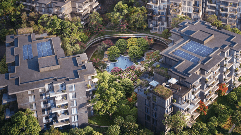 Vue aérienne d'un complexe résidentiel luxueux comprenant plusieurs immeubles d'appartements modernes, dotés de panneaux solaires sur les toits. Le complexe est entouré d'une verdure luxuriante, d'arbres et de jardins paysagers nichés dans les bois sereins de Ghaf, comprenant un plan d'eau central avec des plantes à fleurs vibrantes.