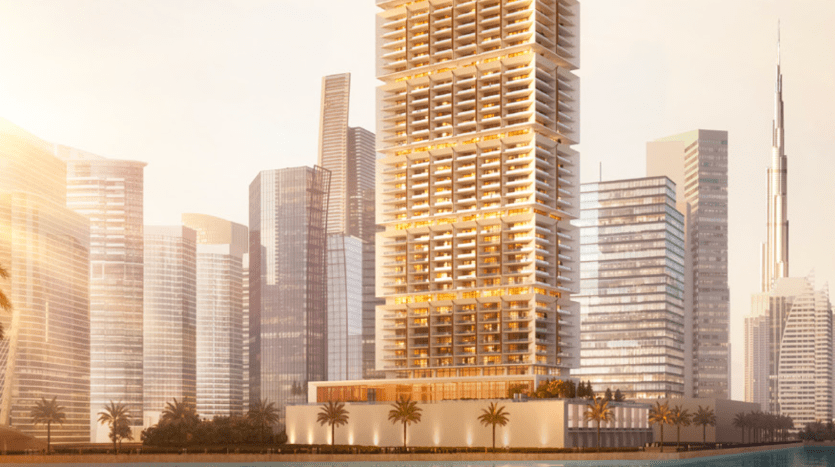 Un moderno paesaggio urbano composto da un gruppo di grattacieli con esterni in vetro riflettente. The One by Binghatti, un grande edificio dal design unico con sezioni a più livelli, si staglia in primo piano accanto a uno specchio d'acqua, circondato da palme e adiacente ad altri grattacieli.