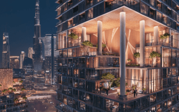 Une vue nocturne d'un immeuble moderne de grande hauteur avec de grandes fenêtres éclairées présentant un intérieur luxueux avec de la verve, des plantes et un décor élégant. Le paysage urbain environnant en arrière-plan présente des gratte-ciel, dont un avec une haute flèche distincte.