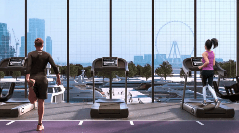 Two people run on treadmills in a modern gym with large windows. The view outside reveals an urban landscape with skyscrapers, greenery, boats and a Ferris wheel in the background. The man on the left is wearing black and the woman on the right is wearing pink.