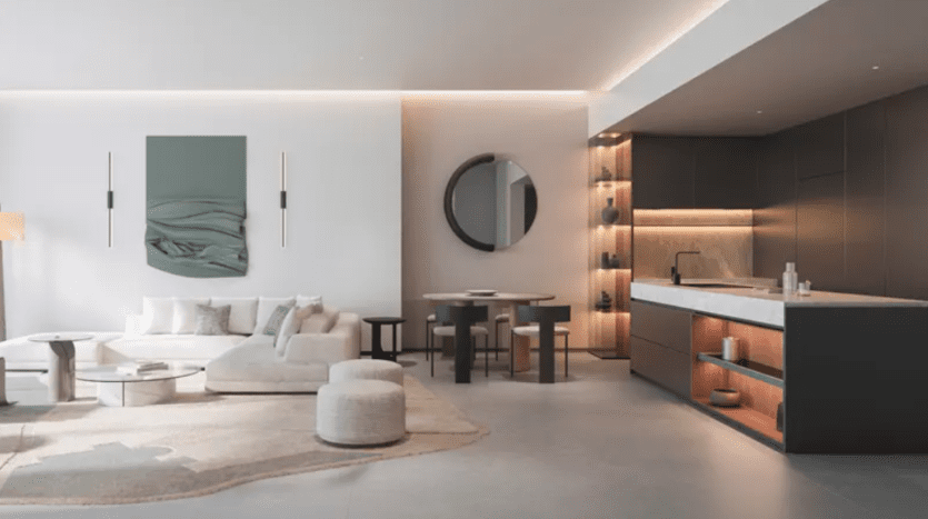 A modern, minimalist open-plan living room and kitchen. The space features a white sectional sofa, a round table with chairs and built-in dark cabinetry with open shelving. The walls are light in color with contemporary art and a circular mirror adorning them.