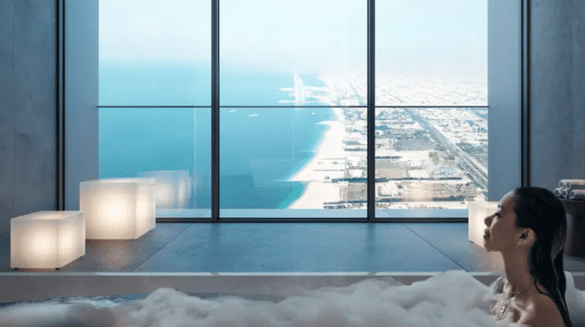 One person relaxes in a modern bathtub filled with bubbles, facing a large bay window offering a breathtaking view of the coastline, the sprawling city next door and the blue sea stretching to the horizon under a clear sky.