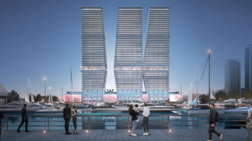 A modern waterfront scene at dusk features two tall, identical buildings with horizontal lines forming a V-shape. People socialize along the promenade, with yachts moored in the marina in the foreground. The area is illuminated by mood lighting.
