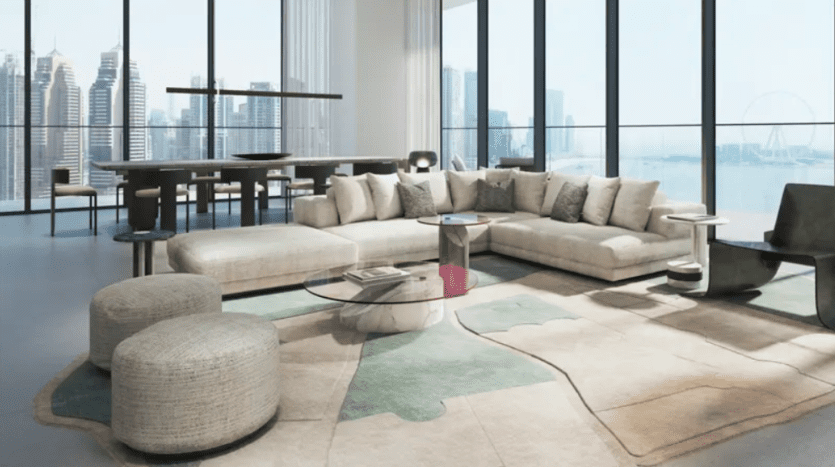 A modern living room with bay windows overlooking a cityscape and Ferris wheel. The room features a large U-shaped beige sofa, two round poufs, a glass coffee table and an abstract-patterned rug. A dining table can be seen in the background.