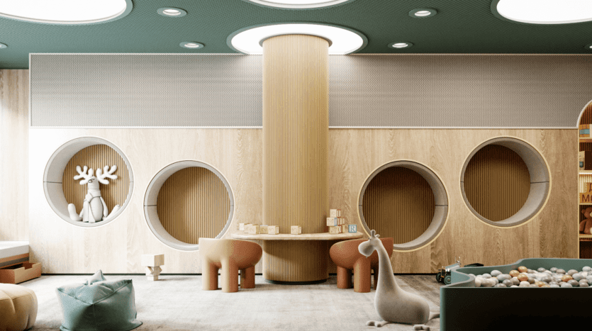 A modern children's playroom, inspired by The Pier, features a large central pillar, circular wall corners and playful furniture. The room features soft lighting, plush seating and a variety of toys, including blocks and a ball pool. Whimsical stuffed animals and reindeer decor add charm.