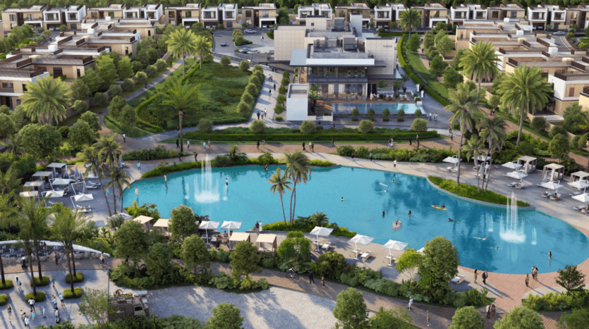 Vue aérienne du complexe Sobha Elwood avec une grande piscine bleue entourée de fontaines, de palmiers et de chaises longues. De nombreux bâtiments modernes et un aménagement paysager luxuriant peuvent être vus autour de la piscine. Les gens se détendent et profitent des commodités.