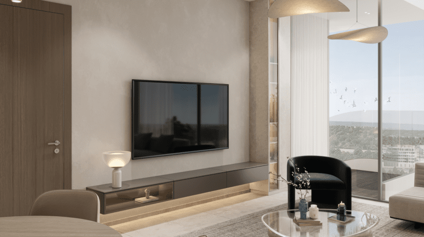 Un salon moderne dispose d'un grand téléviseur fixé au mur, à côté d'un élégant meuble REEF 1000 avec une lampe. Un fauteuil vert foncé et une table ronde avec des objets décoratifs complètent le décor. Une grande fenêtre offre une vue sur le paysage urbain, tandis que des luminaires contemporains sont suspendus au-dessus.