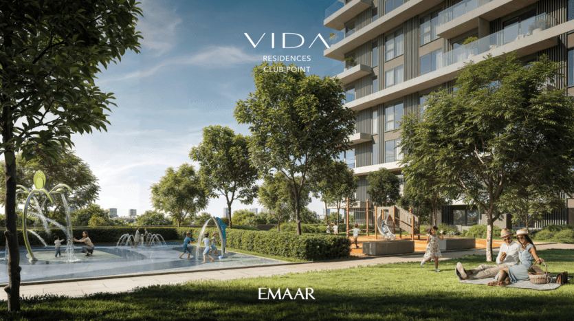 The Vida Residences, a modern apartment building with balconies, overlooks a landscaped garden. People sit and relax on the grass, while children play near a small water feature. Trees and shrubs surround the area, creating a tranquil, verdant environment.