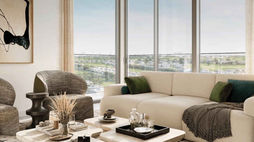 In the elegant Vida residences, the modern living room features a large beige sofa adorned with green cushions and plaid. Two patterned chairs frame a small, dark table, while a window reveals the picturesque greenery of Club Point. A coffee table with vases, books and mugs completes the warm ambience.