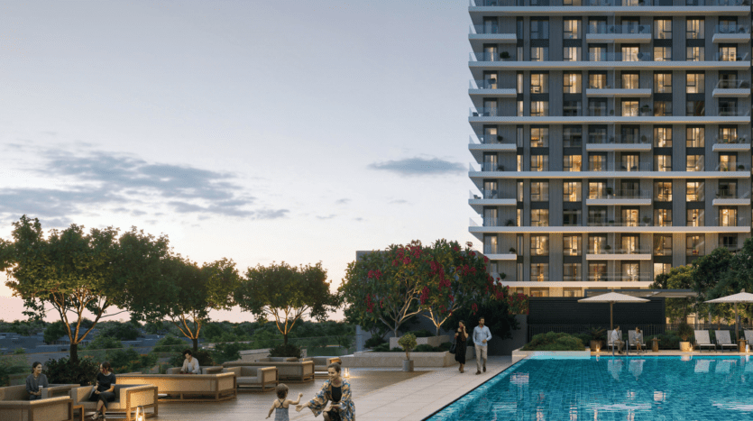 Vida Residences, a modern high-rise building, overlooks a lively poolside area, with people lounging, lush trees and decorative lighting. The sky is clear with soft clouds, hinting at an early evening.