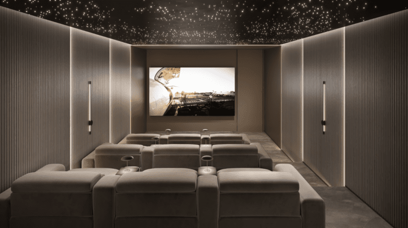 Un home cinéma luxueux avec des fauteuils inclinables moelleux disposés en rangées face à un grand écran diffusant une image panoramique. Les murs sont tapissés de panneaux acoustiques et le plafond présente un effet de nuit étoilée avec de minuscules lumières brillantes.