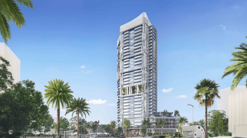 Un immeuble moderne de grande hauteur au design unique se dresse sous le ciel bleu clair le long de la promenade. Entouré de palmiers et de verdure, quelques voitures sont visibles à sa base, créant une atmosphère à la fois urbaine et tropicale.