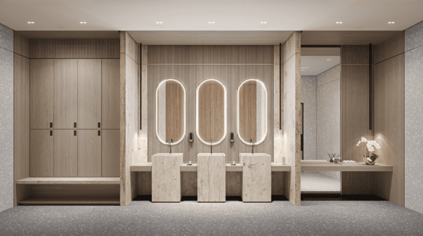 Une salle de bain moderne avec trois miroirs ovales éclairés au-dessus de lavabos en marbre. Les murs et les meubles sont en bois clair. Une plante décorative est placée sur un comptoir élégant à droite. Le design est minimaliste avec une palette de couleurs neutres.