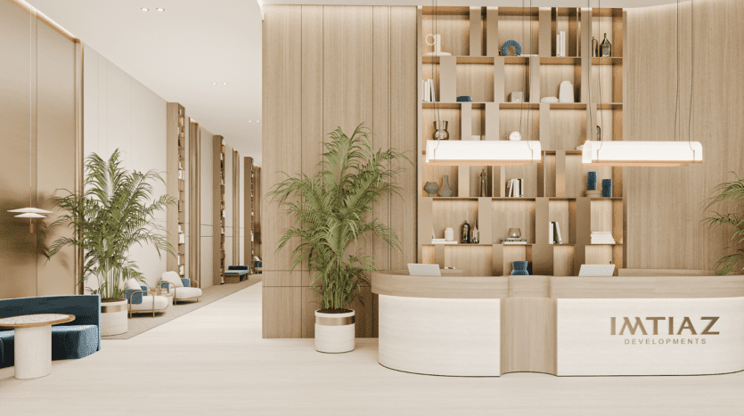 Une réception moderne avec un bureau en bois incurvé, une enseigne "IMTIAZ DEVELOPMENTS", de hautes étagères décorées, des plantes en pot et des sièges élégants le long d'un couloir spacieux et lumineux.