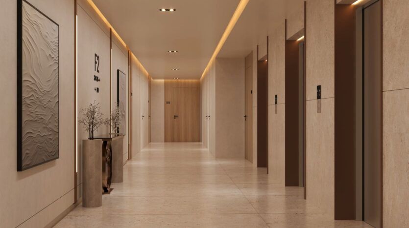 Le couloir moderne et bien éclairé d'Ayaan Heights 1 by IGO présente des murs et des sols beiges, trois portes d'ascenseur sur la droite, des œuvres d'art minimalistes et une table décorative avec des vases et des branches sur la gauche, avec des portes à l'extrémité.