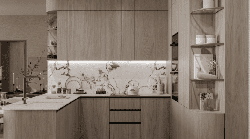 Cuisine moderne avec armoires en bois clair, dosseret et comptoir en marbre, robinetterie dorée, four encastré, étagères ouvertes contenant des objets de décoration et éclairage doux sous les armoires. La vaisselle et les fruits sont soigneusement disposés sur les comptoirs.