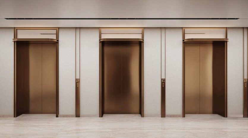 Trois portes d'ascenseur fermées, de couleur dorée, sont encastrées dans un mur de couleur claire avec des garnitures dorées assorties dans le hall moderne du Marquis One Arjan, doté d'un sol en marbre épuré.