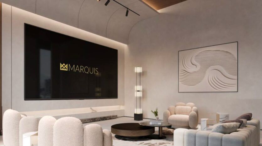 Le salon moderne et élégant du Marquis One Arjan est composé de canapés incurvés de couleur crème, d'une table ronde, de hauts lampadaires, d'un grand écran noir affichant "MARQUIS" et d'œuvres d'art murales abstraites à motifs de vagues. L'espace est légèrement éclairé.
