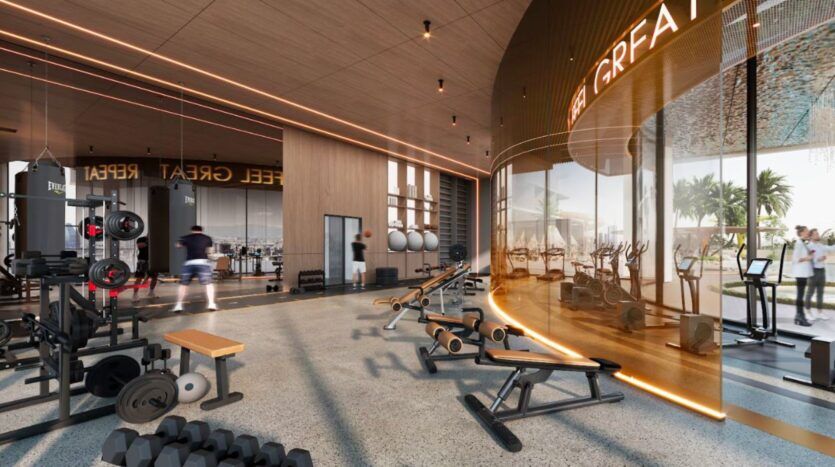 Salle de sport moderne au Marquis One Arjan avec divers équipements d'entraînement, des bancs, des poids et des tapis roulants. De grandes fenêtres inondent l'espace de lumière naturelle. Un éclairage chaleureux et un design épuré créent une atmosphère accueillante pour tous les niveaux de fitness.