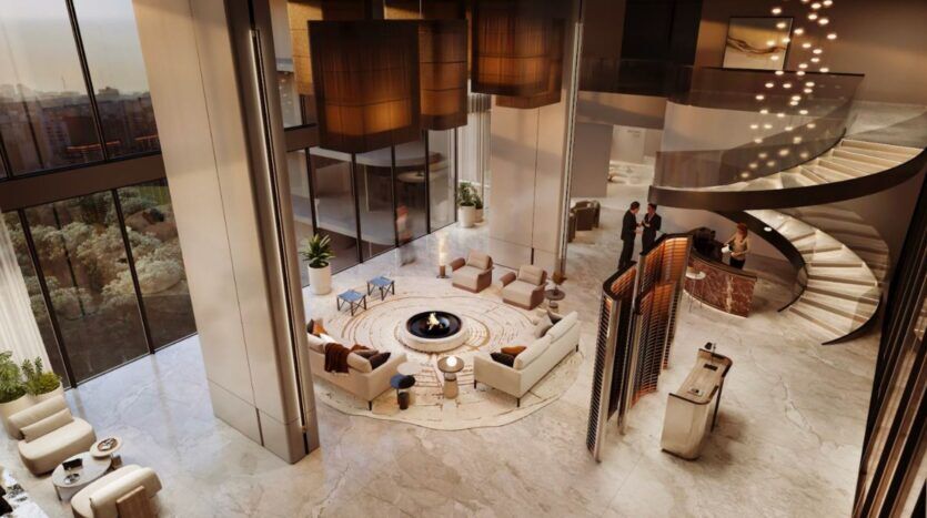 Le luxueux hall d'entrée moderne du Marquis One Arjan est doté de sols en marbre, d'un escalier incurvé, de grandes fenêtres et d'un coin salon central autour d'une table basse ronde et d'une cheminée. Un éclairage chaleureux et une décoration élégante créent une atmosphère accueillante.