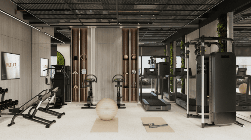 Salle de sport moderne équipée de machines d'exercice, de poids libres, de bancs, de deux vélos d'appartement, d'un ballon de stabilité, de deux tapis et de grands miroirs. L'espace présente des tons neutres, des touches de bois et de la lumière naturelle grâce à de grandes fenêtres.