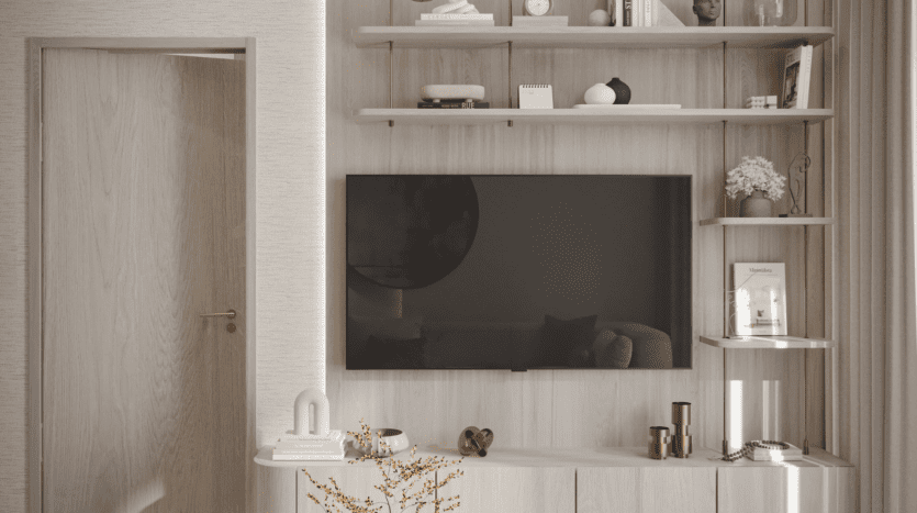 Salon moderne avec des meubles en bois clair, une télévision murale, des étagères décoratives contenant des livres, des vases et des bibelots, et une porte en bois partiellement ouverte sur la gauche. Couleurs chaudes et neutres.