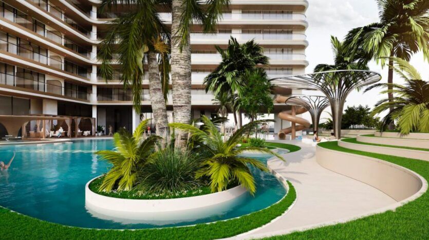 Le Marquis One Arjan est un complexe moderne doté d'une piscine incurvée avec des palmiers, un aménagement paysager luxuriant et un toboggan en spirale près d'un bâtiment à plusieurs étages avec des balcons. Des sentiers pittoresques et des espaces verts entourent la piscine.